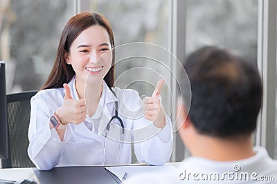 Asian beautiful woman doctor smiles and shows thump up sign or â€œVery goodâ€ with her patient due to his healthcare at hospital Stock Photo